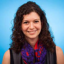 A headshot of Dr. Dalia Rotstein, an MS researcher. She has curly brown hair and is smiling against a blue background.
